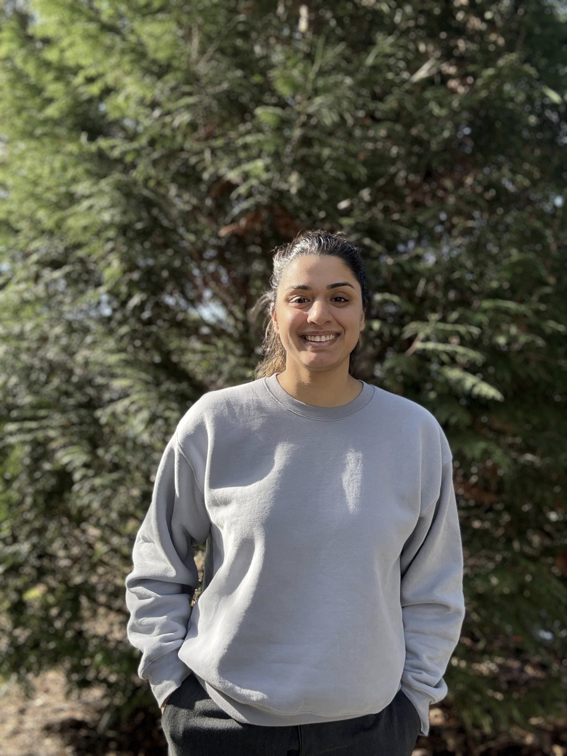 Dr kami smiling in gray sweater among green trees